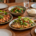 อาหารจานกลางทั้งไก่ย่าง ปลา ผัก และข้าว วางร่วมกับจานส่วนตัวรอบโต๊ะ