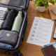 กระเป๋าเดินทางเปิดอยู่พร้อมเสื้อผ้า ร่ม ขวดน้ำ แผนที่ และอุปกรณ์ท่องเที่ยวบนโต๊ะ